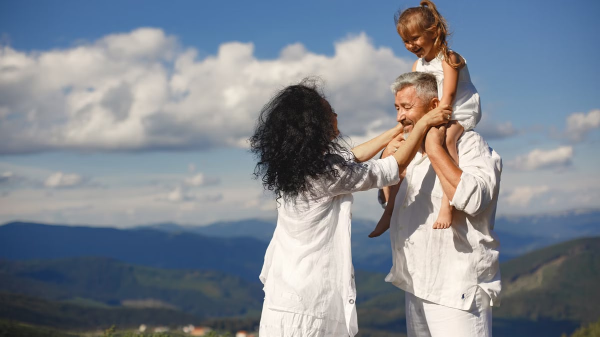 Grandparents with granddaughter having fun in nature. Scenic mountain view and joyful family moment.