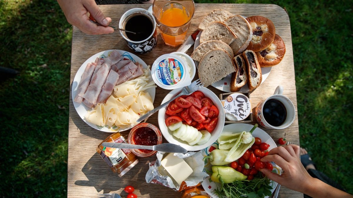 Enjoy a delightful outdoor brunch with bread, cheese, cold cuts, coffee, and fresh vegetables.